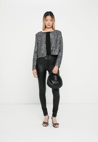 Kort gepailleerde zilveren sequined blazer met knoopsluiting, zwarte top, faux leren broek, zwarte handtas en zwart-witte stippenhakken.