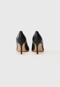 Pair of black leather high-heeled shoes viewed from the back on a plain white surface.