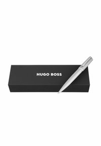 Penna a sfera argentata con impugnatura testurizzata appoggiata su una scatola nera con la scritta "HUGO BOSS" in lettere bianche.