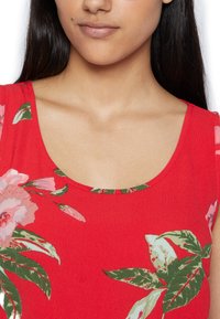 Top de verão floral vermelho com decote redondo e padrões de folhas verdes, feito de um tecido macio com uma textura suave.