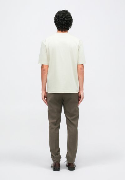 Világos bézs, rövid ujjú póló olíva zöld nadrággal párosítva, laza szabású és sima textúrájú anyagból készült. Barna cipők teszik teljessé az öltözetet.