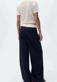 Schwarze, weit geschnittene Hose aus einem glatten Stoff, mit hoher Taille und minimalistischem Design. Die Rückseite verfügt über dezente Taschen und Nähte.