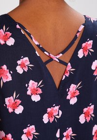 Marineblaues Kleid mit Blumenmuster, das pinke Blumen zeigt; V-Ausschnitt-Design mit überkreuzten Trägern und einer weichen Stofftextur.