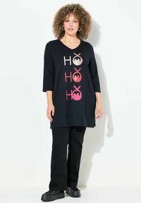 Musta tunika V-pääntiellä, jossa on kolme metalliväriä "HO"-motivia. Yhdistetty mustiin housuihin ja paksupohjaisiin mustiin kenkiin.