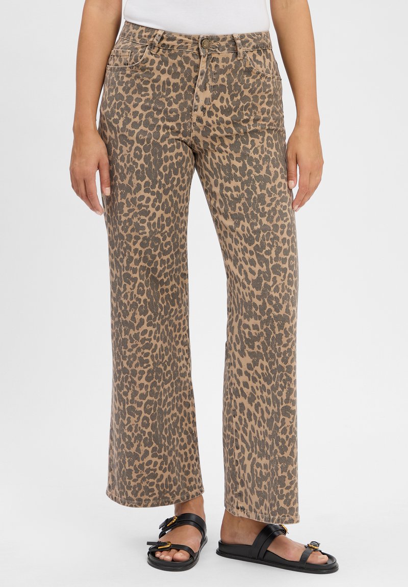 Jean large à imprimé léopard en beige et marron, avec un design classique à cinq poches et une fermeture à bouton. Portés avec des sandales noires.