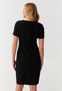 Robe noire à manches courtes, silhouette ajustée, ourlet au genou et détail de fermeture éclair à l'arrière. Tissu lisse avec un léger éclat.
