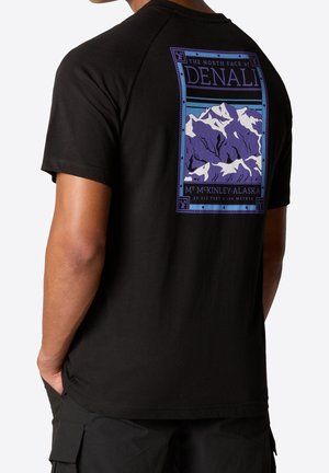 Homme portant un T-shirt noir avec un motif violet et bleu de montagnes enneigées intitulé « Denali Mt. McKinley - Alaska » au dos.