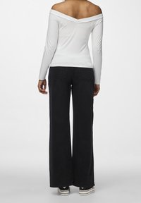 Vit off-shoulder långärmad topp kombinerad med höga, vida svarta byxor och svarta sneakers med vita sålar.