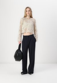 Haut court en dentelle crème avec manches longues, associé à un pantalon noir taille haute et un sac à main noir, présentant un design lisse et structuré.