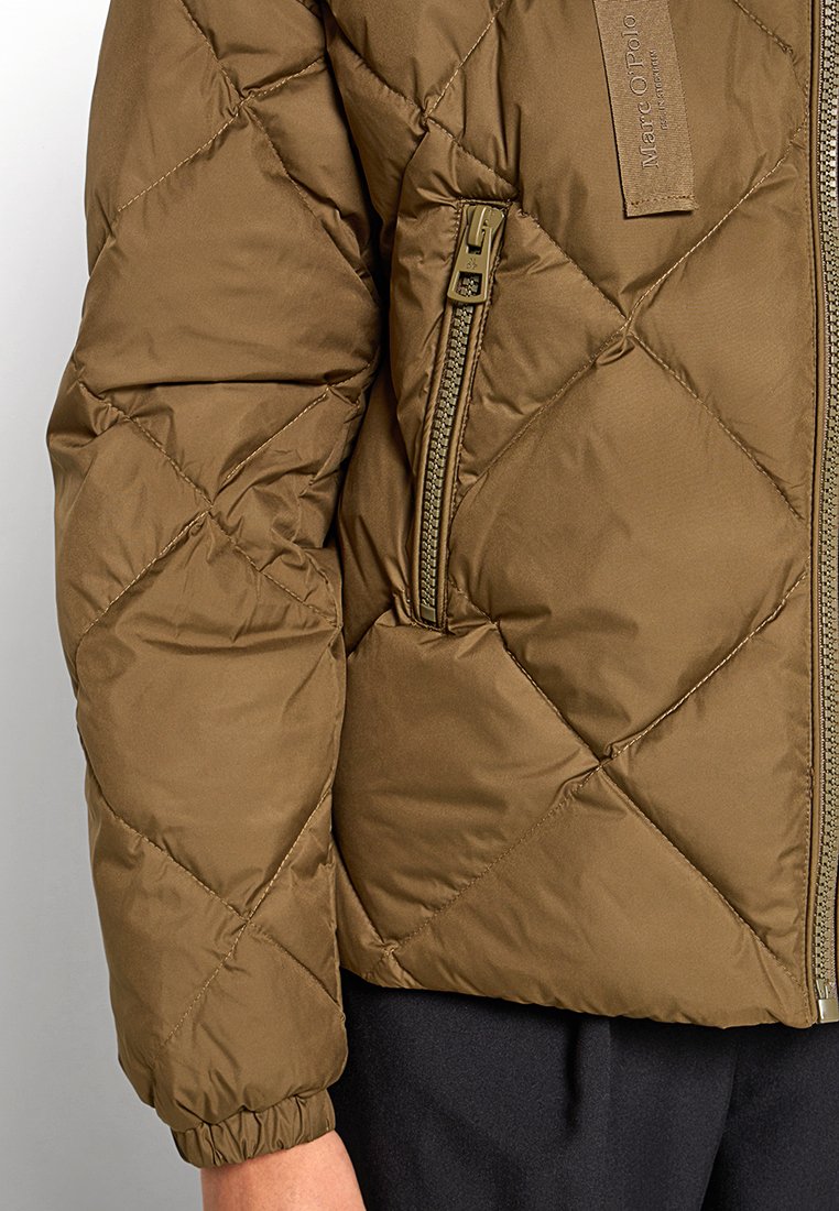 Olijfgroene gewatteerde pufferjas met een gladde textuur, voorzak met rits en een merklabel op de schouder. Voorzien van elastische manchetten en een staande kraag.