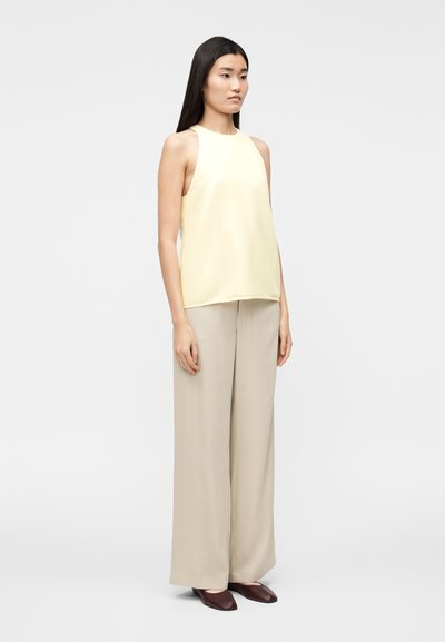 Ανοιχτό κίτρινο αμάνικο τοπ με λεία υφή, συνδυασμένο με μπεζ παντελόνια φαρδιάς γραμμής και σκοτεινά μαρόν μυτερά παπούτσια.