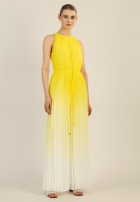 Vestido maxi plisado que transiciona de un amarillo brillante a blanco, con un cuello alto, cintura ajustable con cordón y diseño sin mangas.
