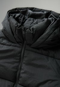 Schwarze Daunenjacke mit hohem Kragen, gestepptem Design und zentralem Reißverschluss. Der Stoff hat einen subtilen Glanz und eine leichte Optik.