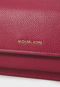 Laukku fuksia nahkaa, jossa on teksturoitu pinta, kultainen "MICHAEL KORS" -logo ja ommellut yksityiskohdat taittuvassa läpäreessä.
