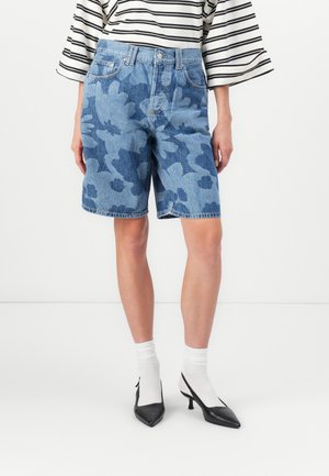 Lichtblauwe denim shorts met een donkerder bloemenpatroon. Heeft een hoge taille, voorkruiden en een gerafelde zoom, gestyled met zwarte hakken.
