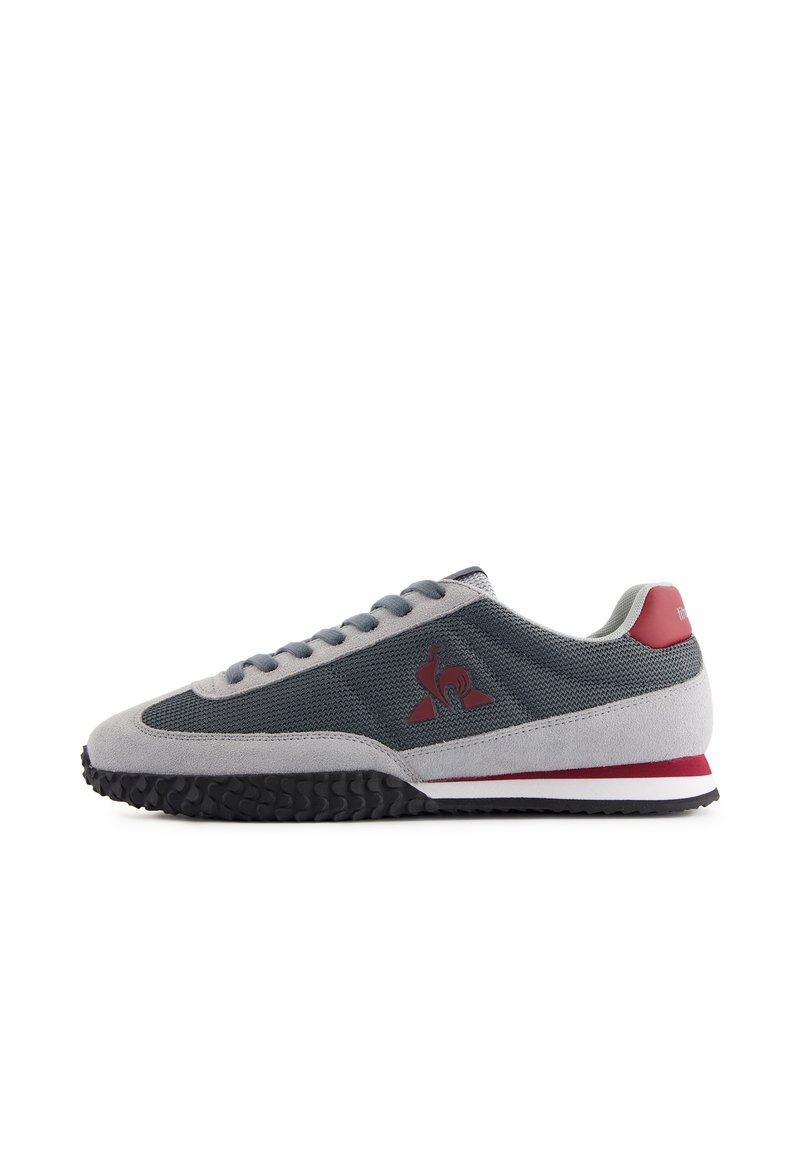 Baskets en suede gris et mesh avec des accents rouges, design à lacets, semelle en caoutchouc texturée et détail de logo sur le côté.