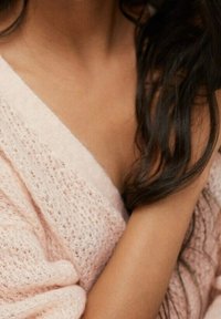 Weicher rosa gestrickter Pullover mit einer lockeren, offenen Maschenstruktur. Die Haare fallen natürlich über die Schulter und unterstreichen den entspannten Look.