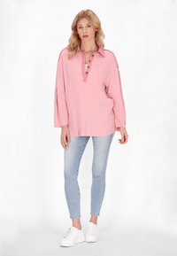 Pullover rosa chiaro con colletto, chiusura a bottoni, fessure laterali e un tessuto testurizzato. Abbinato a jeans skinny blu chiaro e sneakers bianche.