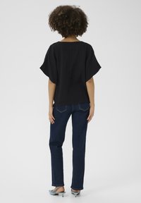 Fekete, rövid ujjú blúz texturált felülettel, sötétkék egyenes szárú farmerral és világoskék magassarkú papuccsal párosítva.