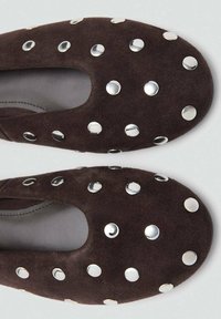 Zapatos de ante marrón sin cordones con punta redondeada, decorados con tachuelas plateadas circulares distribuidas uniformemente por toda la superficie superior.