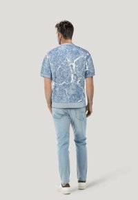 Maglione blu a maniche corte con un motivo marmorizzato, colletto e orlo a coste. Indossato con jeans azzurri chiari e sneakers bianche.
