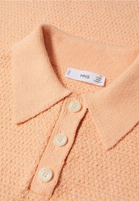 Polo de couleur pêche avec un tissu texturé, doté d'un col et de trois boutons. Étiquette visible avec le nom de la marque MNG.