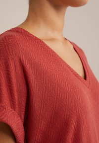 Top rouge à manches courtes avec décolleté en V et un motif en tricot texturé avec de délicates ondulations. Encolure centrée et tissu doux.