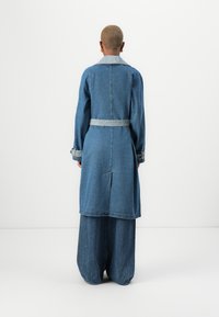 Denim long coat with a lighter denim collar, belted waist, and wide sleeves. The coat has a straight cut and a back vent for movement.