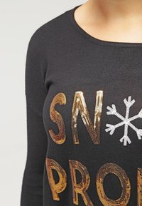 Černý svetr s textem zlatými flitry "SNOW PROBLEM" a bílým sněhovým vločkem, s měkkou texturou a kulatým výstřihem.