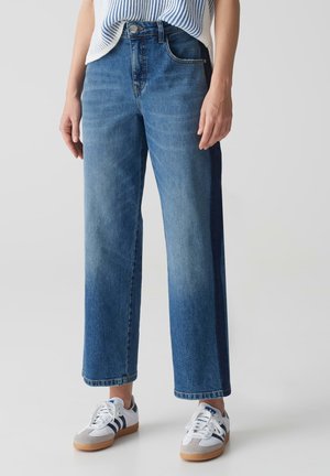 Light blue wide-leg jeans with faded texture, high waist, and classic five-pocket design. Paired with white sneakers featuring navy accents.