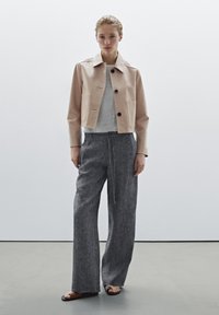 Cropped beige leather jacket with large front pockets, gray T-shirt, loose gray linen trousers, and black sandals. Simple, clean design.