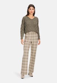 Olivgrüner, gestrickter Pullover mit lockerer Passform und V-Ausschnitt. Kombiniert mit hochtaillierten Karohosen in Beige- und Brauntönen, die ein gerades Bein haben.