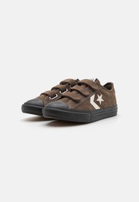 Zapatillas de ante marrón con suelas de goma negras, que cuentan con dos tiras de Velcro y un acento de estrella blanca en el costado. Diseño de punta redonda.