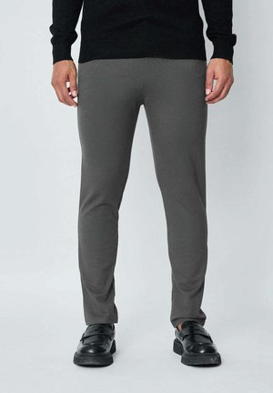 Pantalons gris ajustés en tissu lisse. Dotés d'une taille standard et de poches latérales, associés à des chaussures noires.