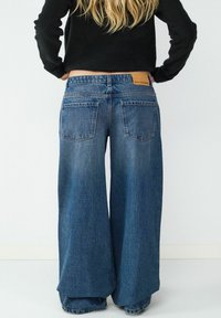 Jeansy z szerokimi nogawkami w średnim zmyciu, z wysokim stanem, skórzaną łatą z logo na plecach oraz minimalnymi detalami w tylnej kieszeni.