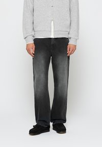 Svart denimjeans med en falmet finish, rett snitt og fem-lomme-design, kombinert med en grå ribbestrikket zip-up genser og svarte slip-on sko.