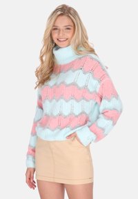 Pastelblauwe en roze trui met zigzagpatroon, gebreide textuur en coldesign; gecombineerd met een beige minirok.