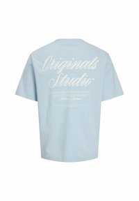 Svetlomodré bavlnené tričko s krátkymi rukávmi, na zadnej strane s bielym textom vrátane "Originals Studio" a s ďalšími detailmi nižšie.