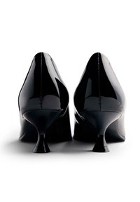 Zapatos de tacón alto de charol negro con punta afilada y un exclusivo tacón en forma de reloj de arena. Acabado liso y brillante con pespuntes en contraste.