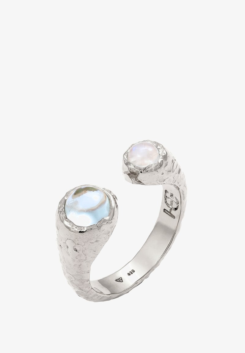 Bague en argent avec un anneau texturé, présentant deux pierres iridescentes—une bleue et une blanche—serties dans des sertissages uniques en forme organique.