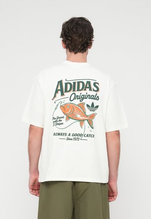 T-shirt branca de algodão com estampa gráfica de um peixe e o texto "Adidas Originals" nas costas. Mangas curtas e corte descontraído.