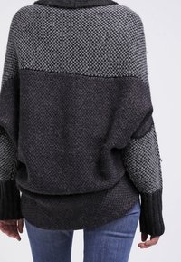 Oversized, stickad tröja i mörkgrått och svart. Har ett strukturerat mönster, vida ärmar och en lös passform med hög krage.