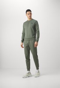 Felpa verde oliva e pantaloni jogger abbinati in tessuto morbido, con polsini e vita a costine, e un piccolo logo sul petto.