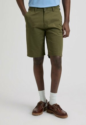 Pantalones cortos de algodón verde oliva con diseño de múltiples bolsillos, trabillas para cinturón y una textura suave, combinados con zapatos de cuero marrón y calcetines gris claro.