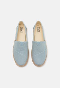 Lyseblå kanvas slip-on sko med teksturert overflate, elastisk V-insert og en såle som ligner på jute. Har TOMS-logo på innersålen.