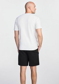 Biała koszulka z krótkim rękawem i okrągłym dekoltem, zestawiona z czarnymi szortami z tylną kieszenią i gładką fakturą materiału.