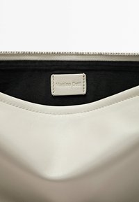 Borsa in pelle di un beige chiaro con una texture liscia. Presenta una zip superiore e un'etichetta cucita con la scritta "Massimo Dutti" in una palette di colori a contrasto.