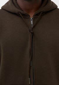 Felpa con zip di colore marrone, dotata di cappuccio regolabile con cordino, caratterizzata da una superficie liscia e una chiusura lampo in metallo. Design semplice, senza motivi.