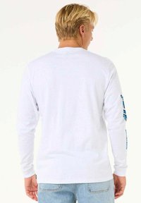 Hvid langærmet t-shirt med rund hals, blå grafisk detalje på venstre ærme og et almindeligt fit design. Materialet ser blødt ud.