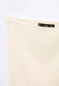 Ribattut cream-colored neulottu kangas, jossa on leveä kaula-aukko. Musta tuotemerkki, jossa on kokotiedot ja hoito-ohjeet.